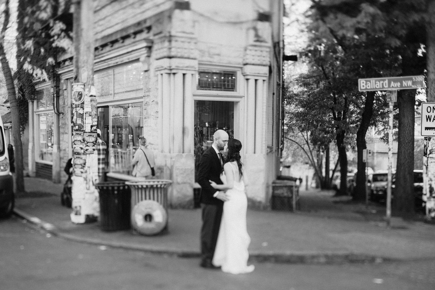 Black and white photo of newlyweds posing in front of a historic storefront on a city street.