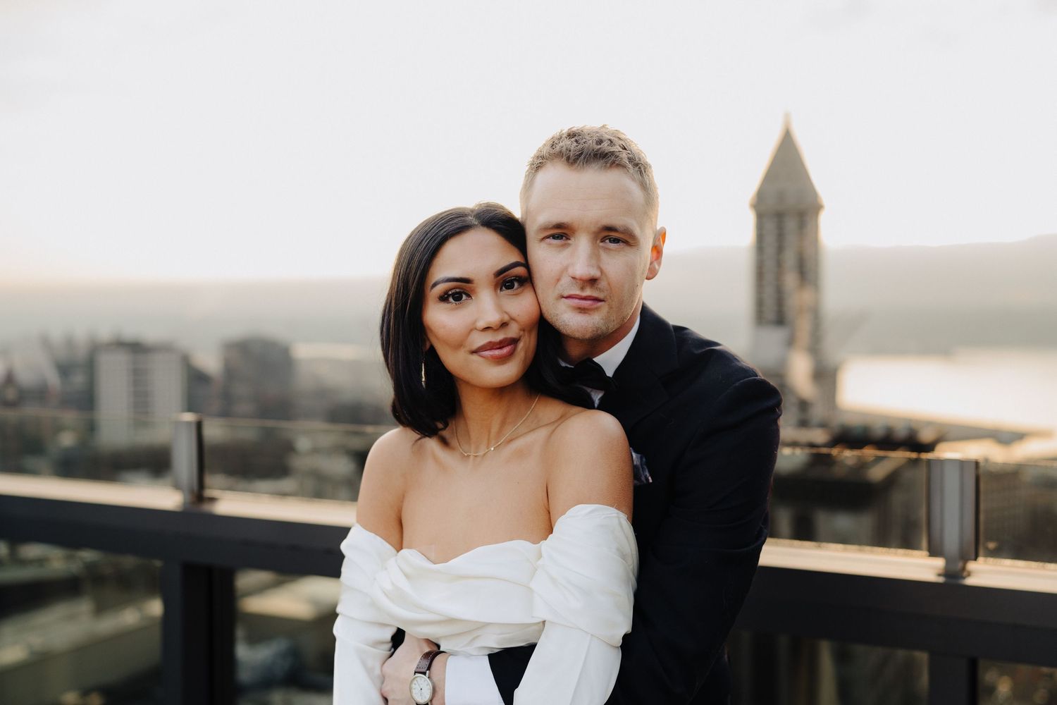 Stylish couple poses together on urban rooftop with historic tower visible in background.