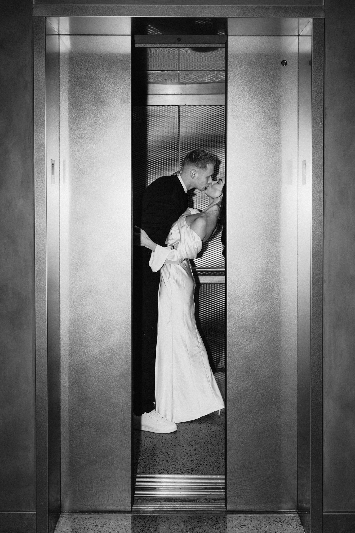 Black and white photo of newlyweds kissing in elevator doorway.