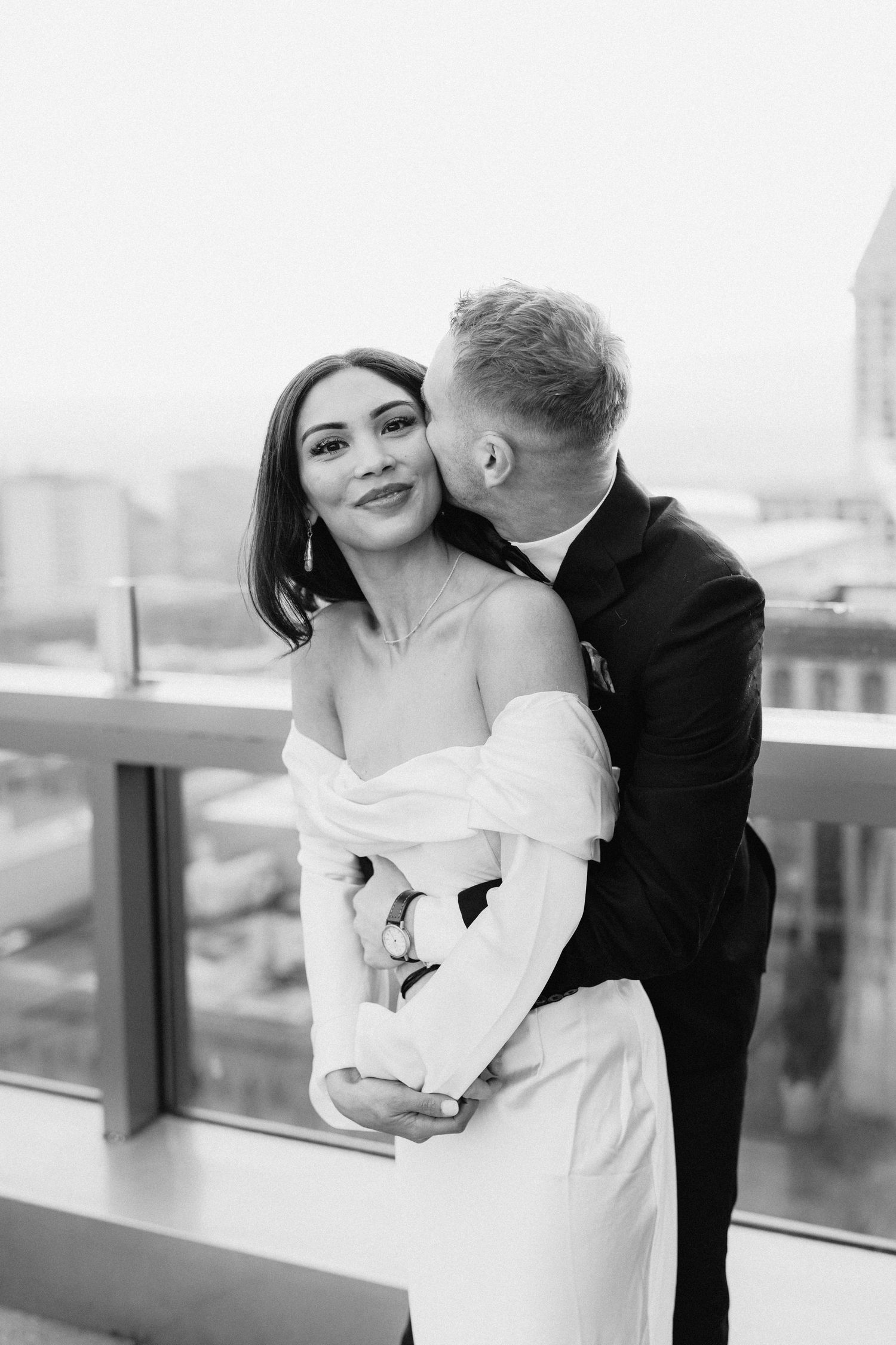 A romantic black and white wedding photo of a couple embracing on a city balcony.