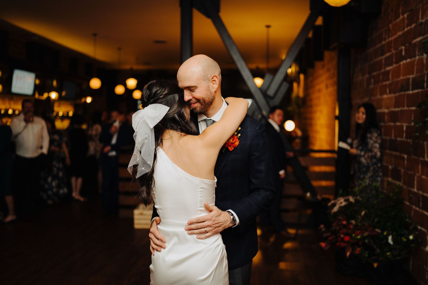 Couple slow dancing in dimly lit venue with exposed brick walls and hanging lanterns.