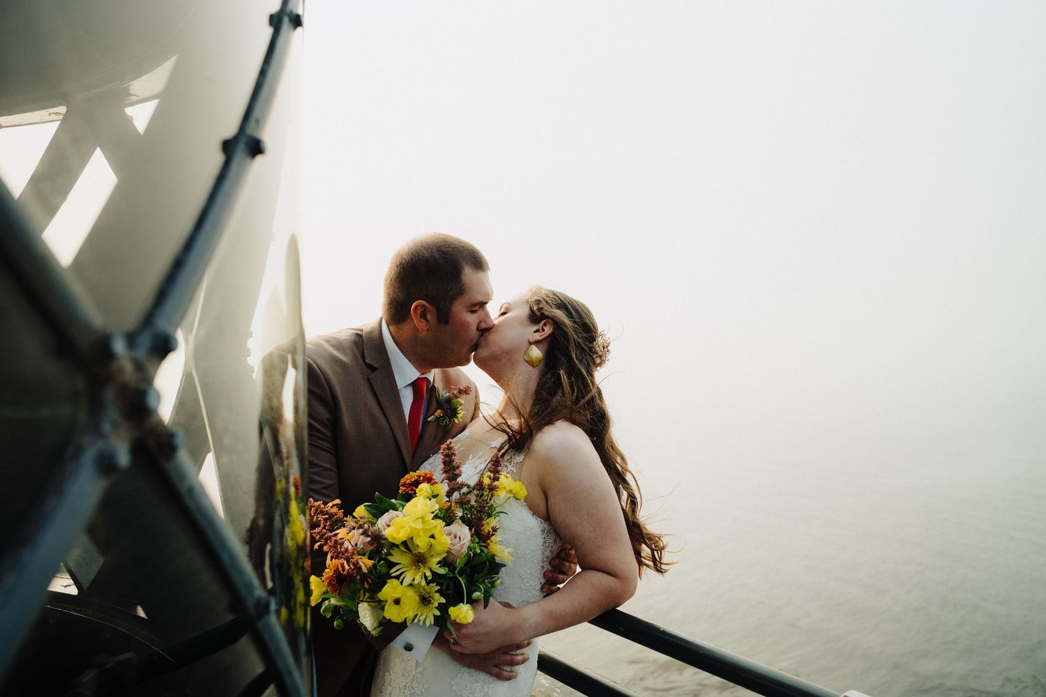 Couple shares a kiss while holding vibrant yellow bouquet inside lighthouse tower.