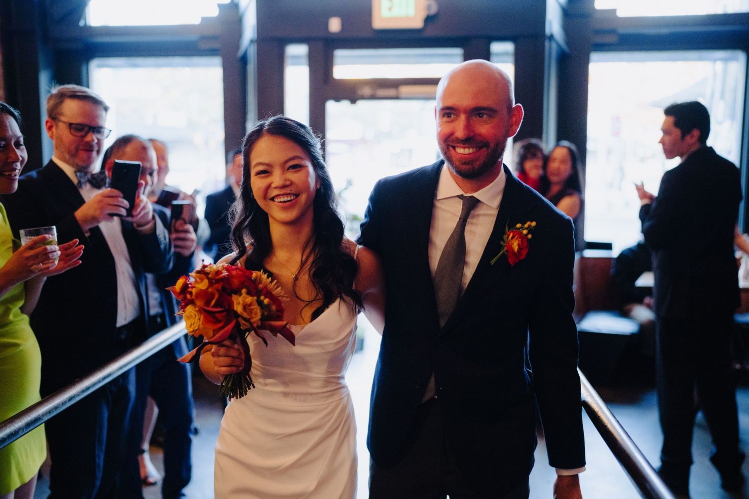 Wedding couple walking down aisle with bride holding orange bouquet.