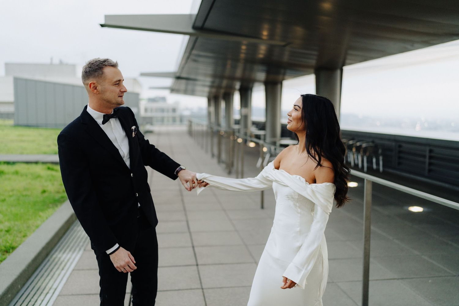A playful moment between bride and groom on an outdoor terrace with cloudy skies.