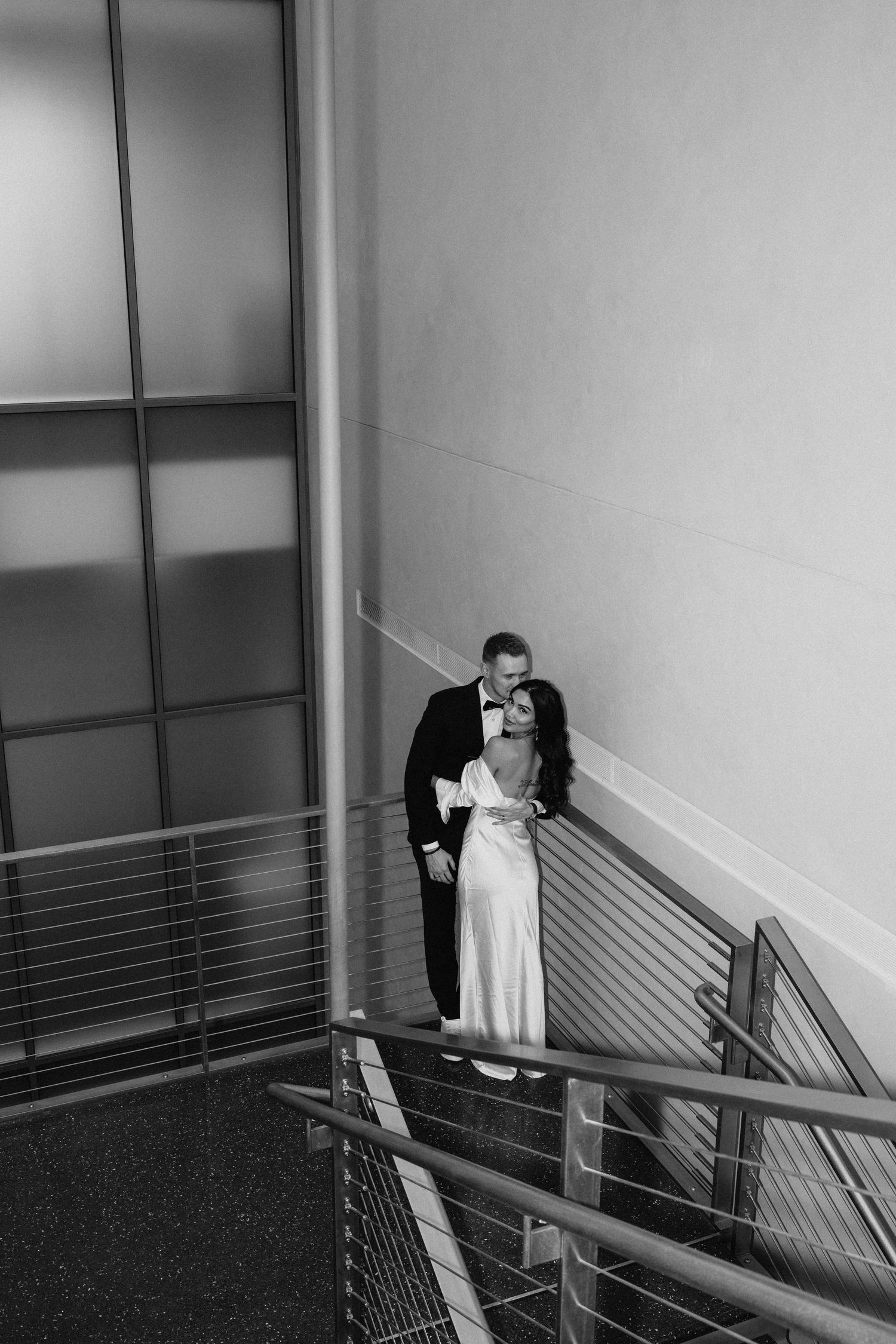 A romantic black and white moment between newlyweds in a modern stairwell with metal railings.
