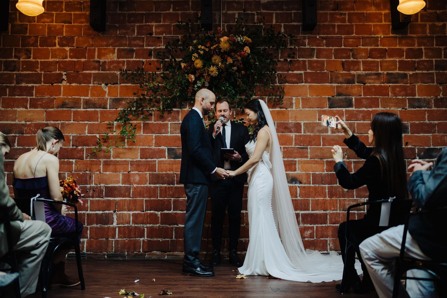 Wedding ceremony with officiant and couple in front of exposed brick wall.