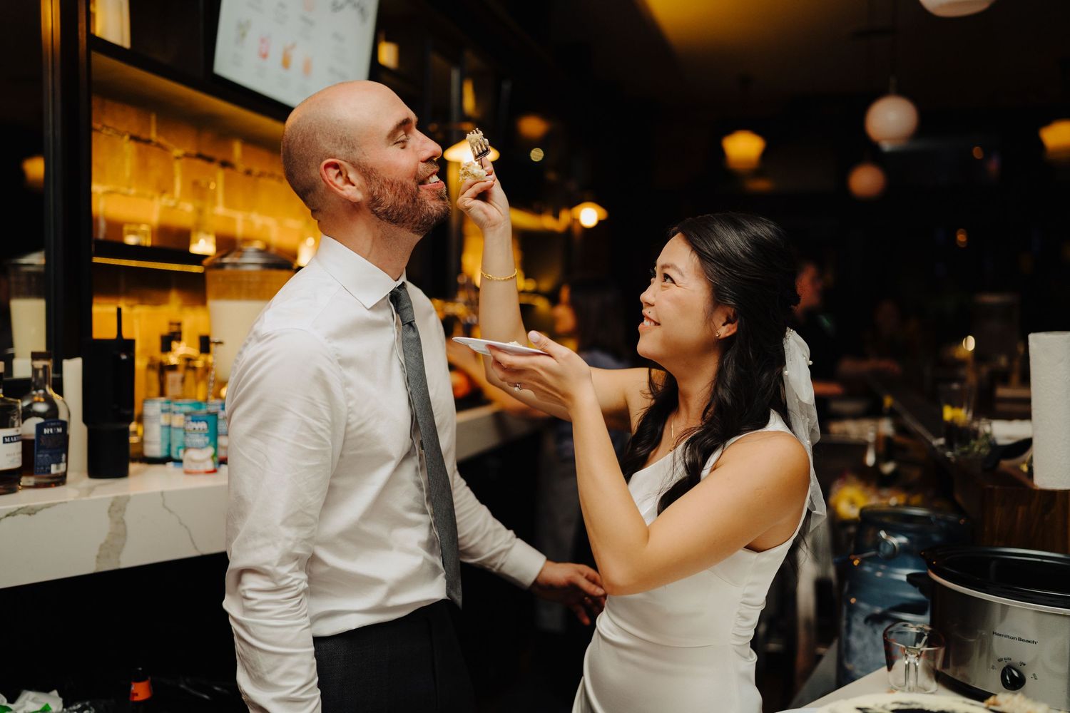 Playful moment between couple during wedding reception at bar.