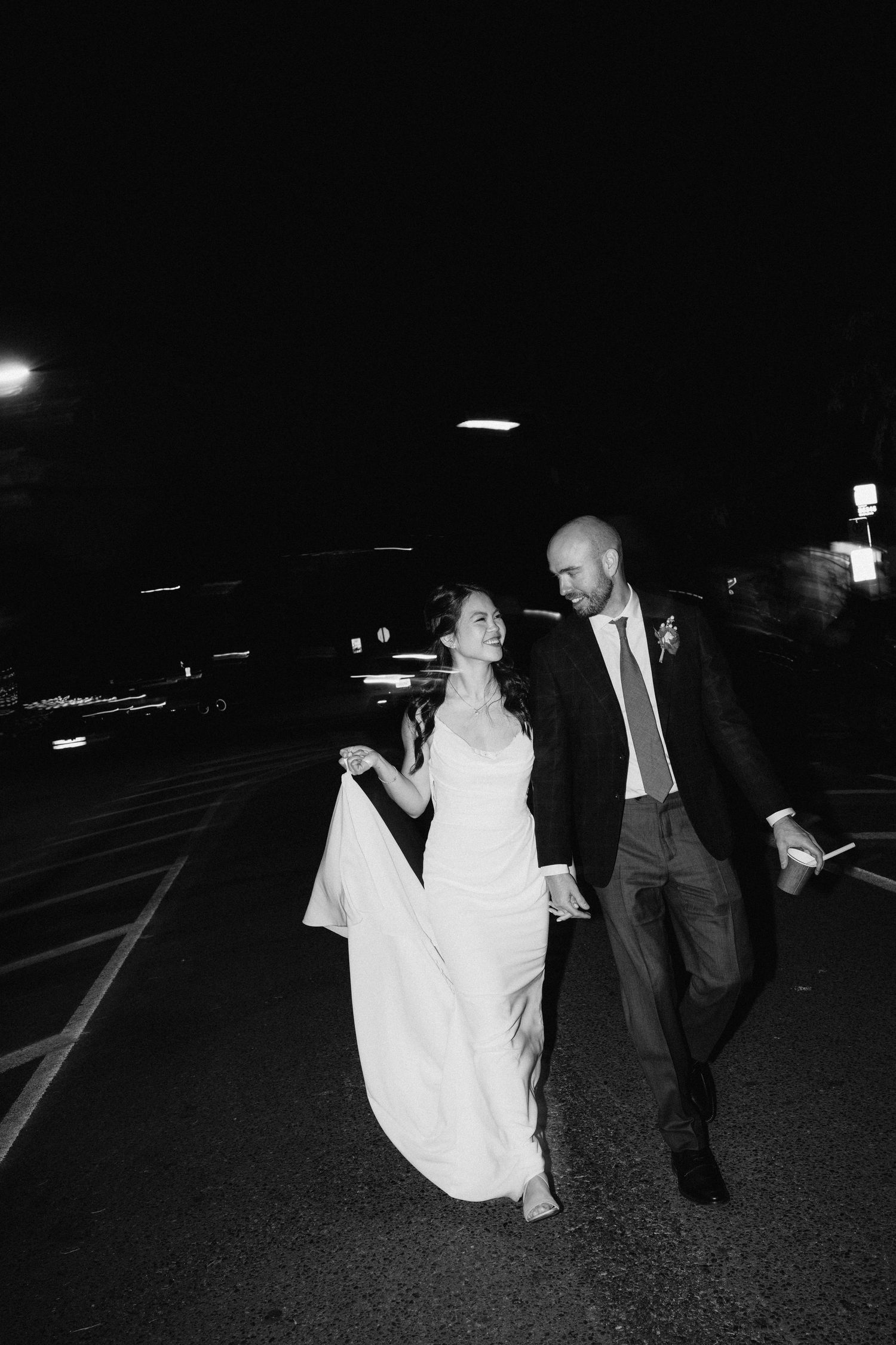 A couple walking through a dark parking lot after their wedding celebration.