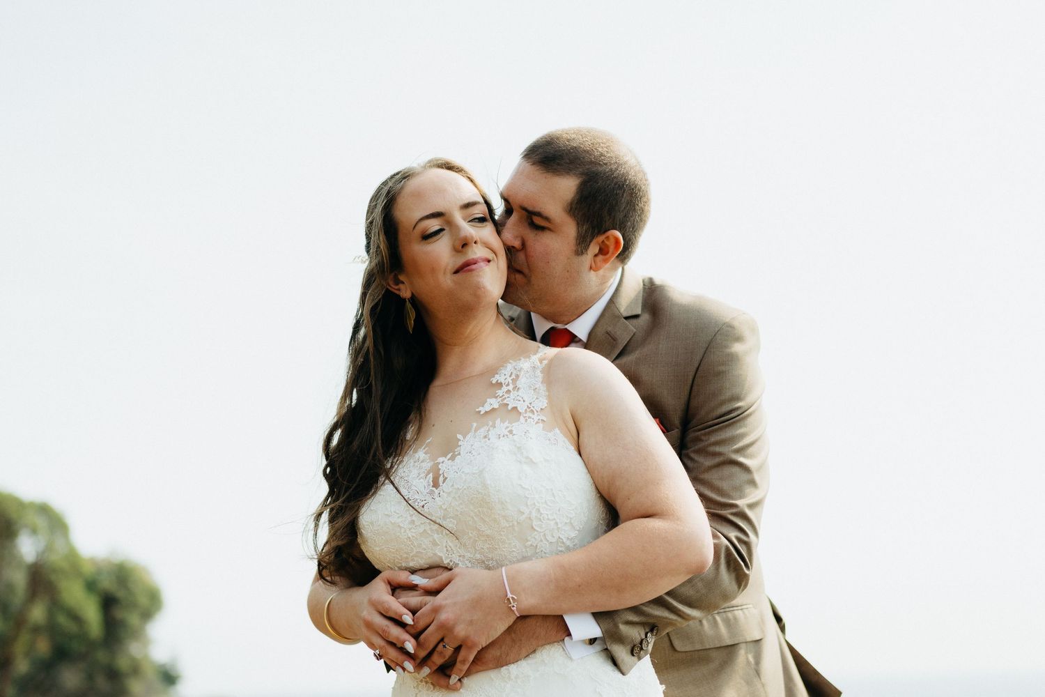 A romantic moment between newlyweds as they embrace outdoors in wedding attire against a soft natural background.