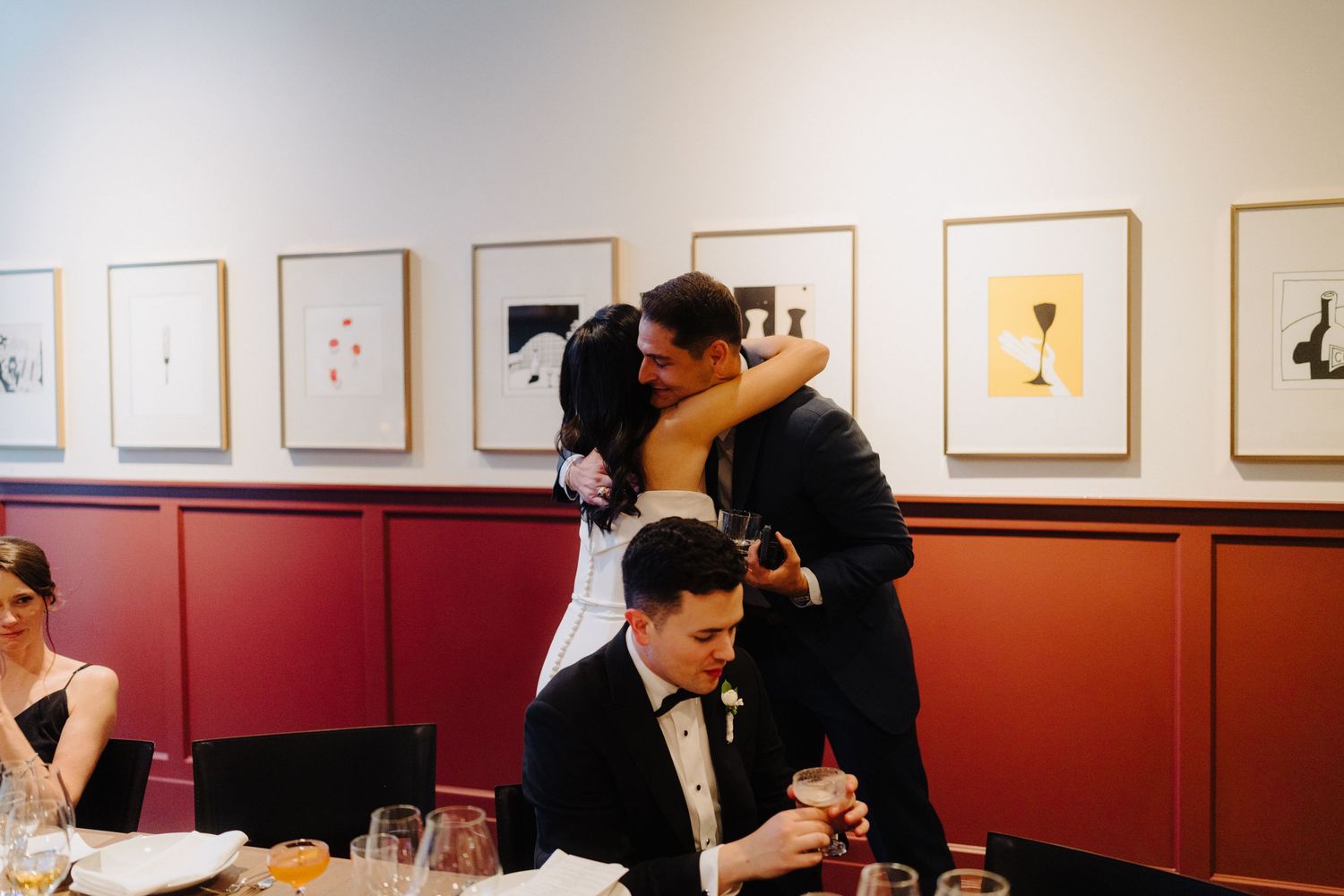 A celebratory moment during a wedding reception with framed artwork on red walls.