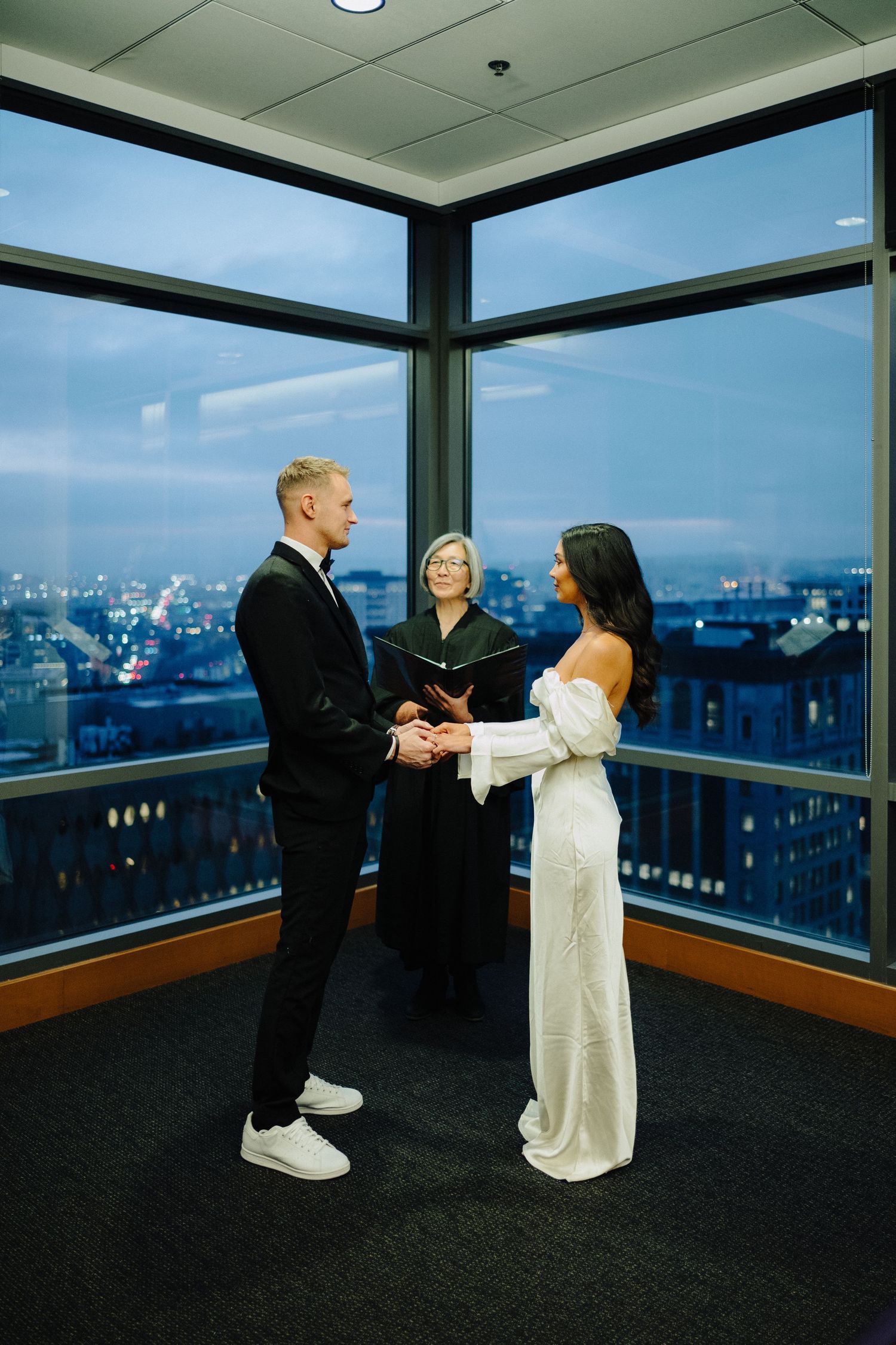 An intimate wedding ceremony with a couple and officiant against a blue twilight city view.