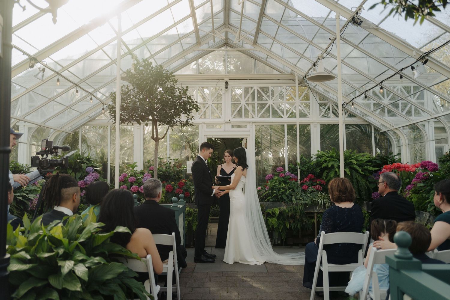 A greenhouse wedding ceremony with white chairs and tropical plants creating a magical atmosphere.