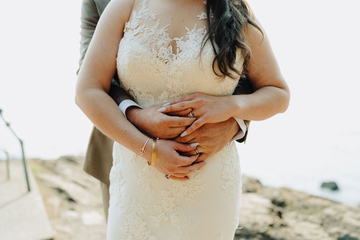 Close-up detail of hands embracing over a lace wedding dress.