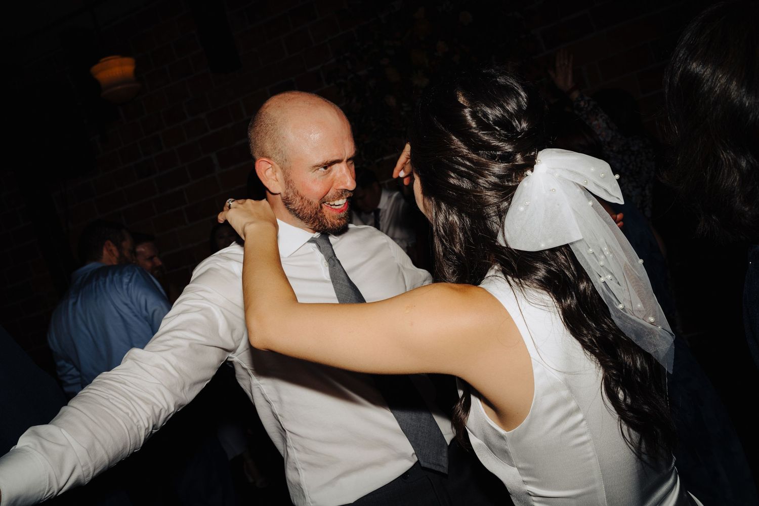 A couple sharing an energetic dance moment at a reception in a dimly lit venue.