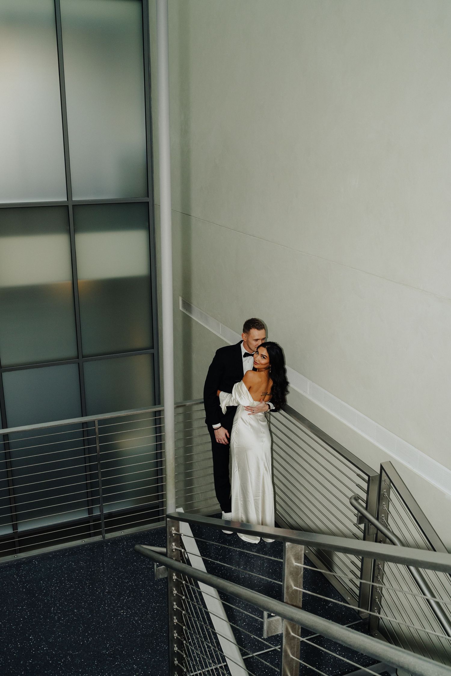 A couple in formal wear sharing a tender moment on a modern staircase.