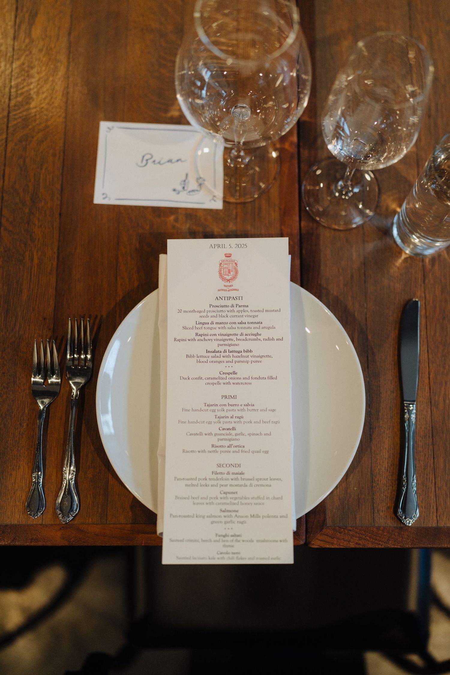 An elegant place setting with wine glasses and a formal menu card on a wooden dining table.
