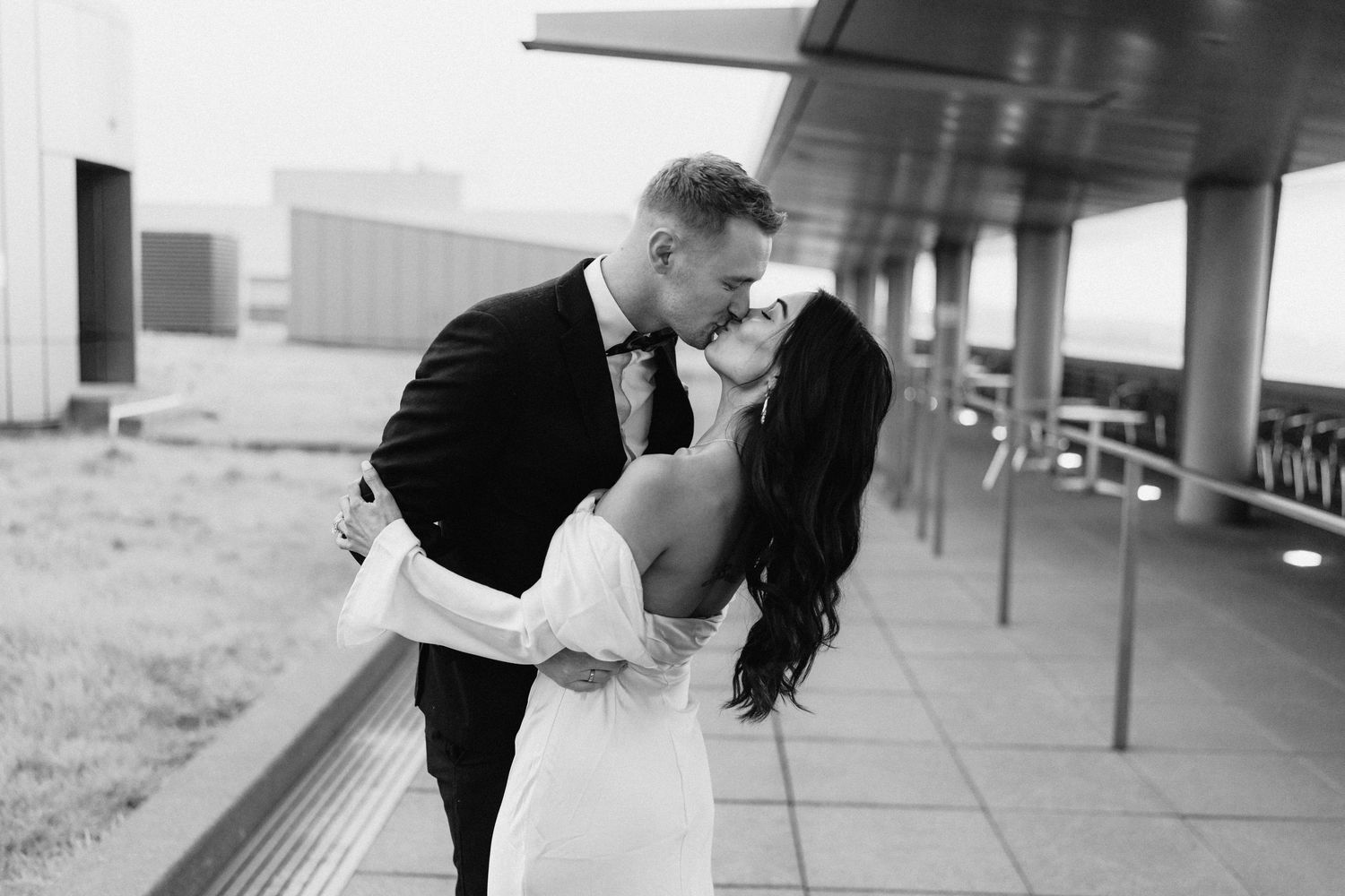 Black and white romantic dip pose of wedding couple on outdoor terrace.