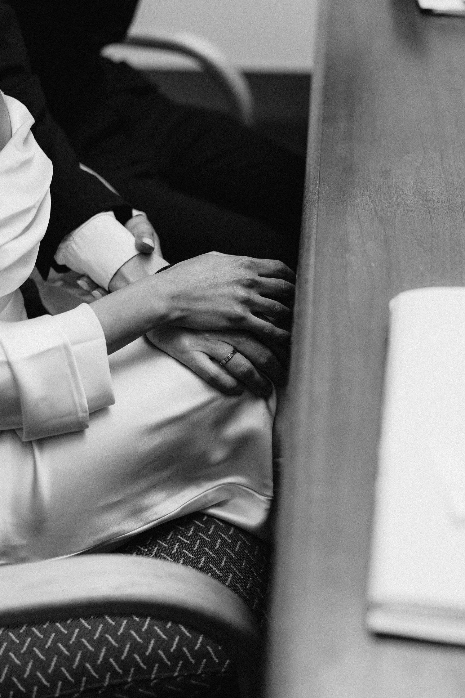 Close-up black and white shot of hands resting on a table during a wedding ceremony.