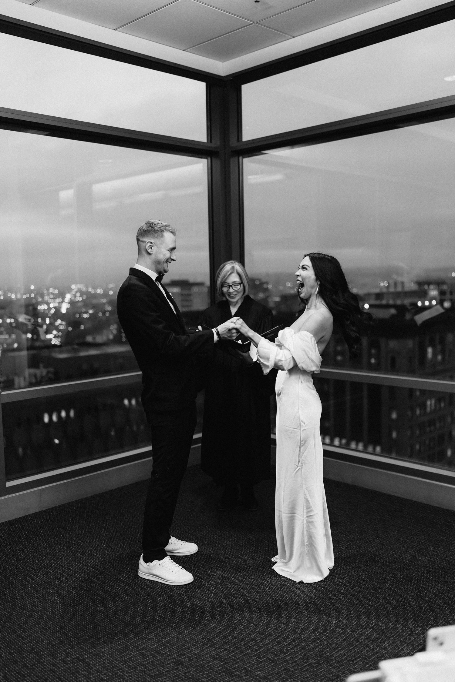 Black and white wedding ceremony photo in modern high-rise venue with city views.