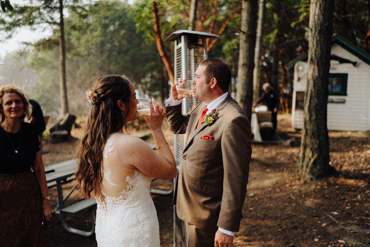 A couple shares a toast together during their wedding reception in a wooded outdoor setting.