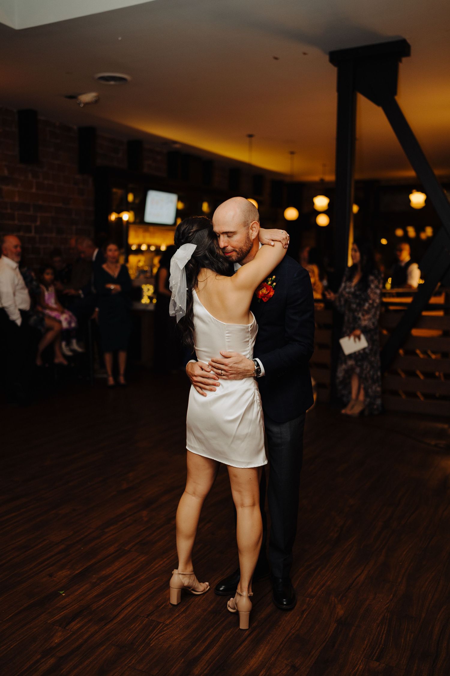 Couple shares an intimate dance together on a dark wooden floor under warm ambient lighting.