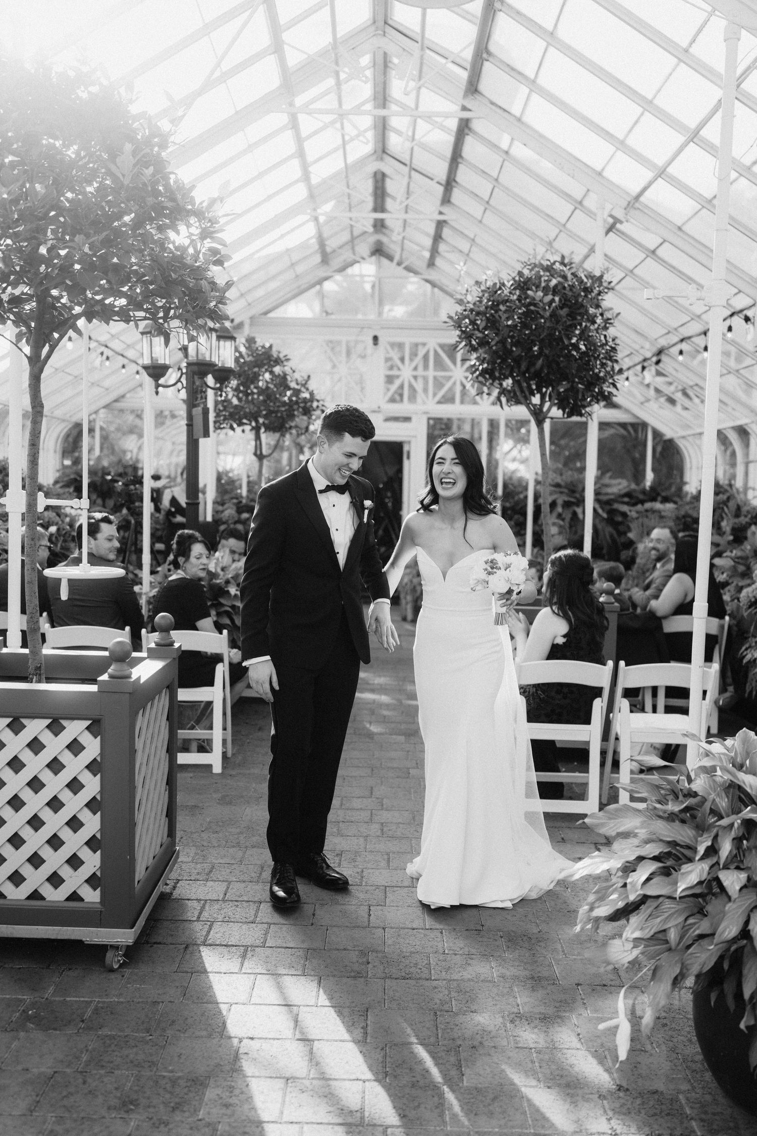 Black and white photo of a wedding couple sharing a moment in a sunlit greenhouse.