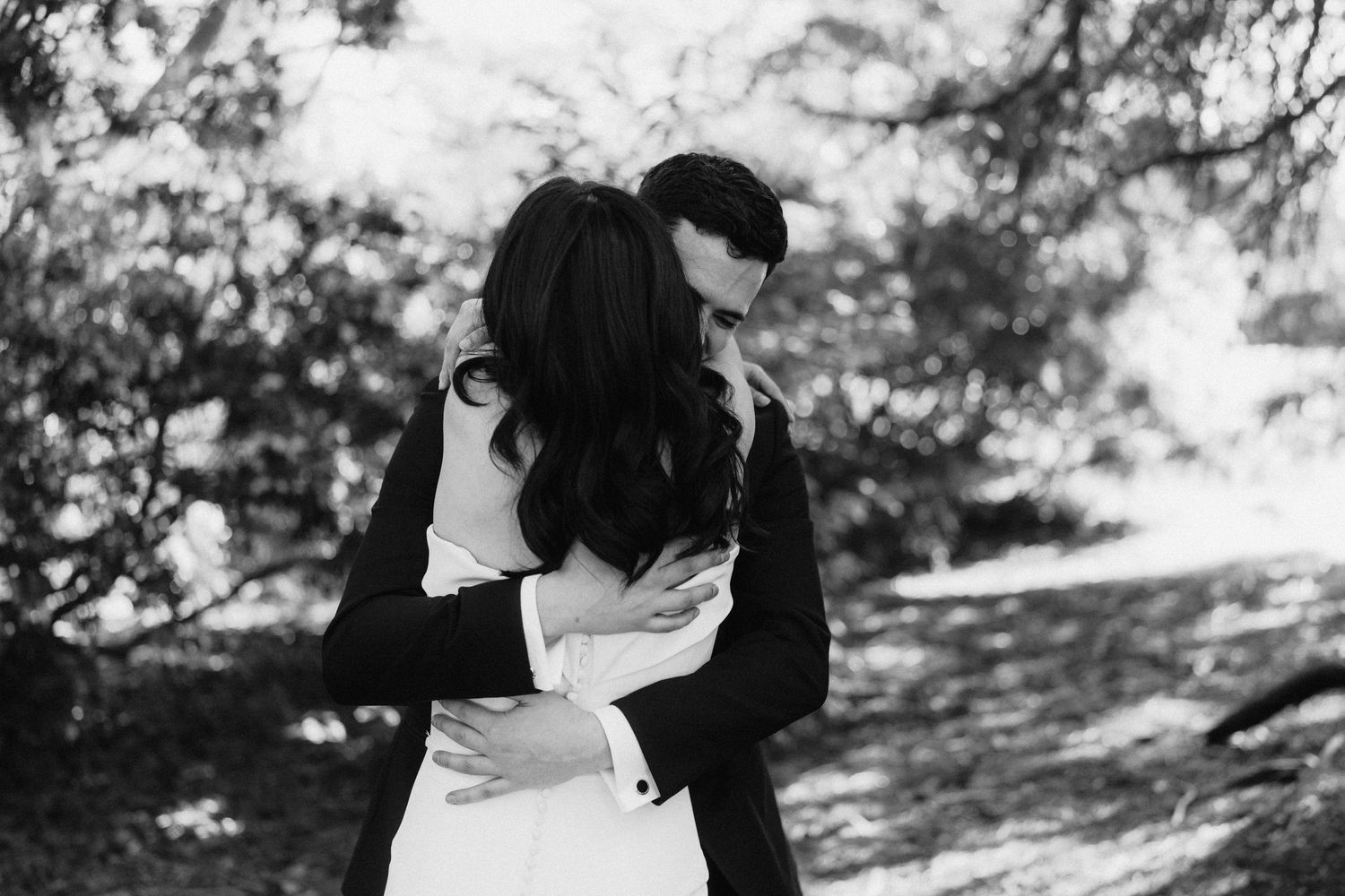 A black and white romantic photograph of an intimate embrace between a couple outdoors in a natural setting.