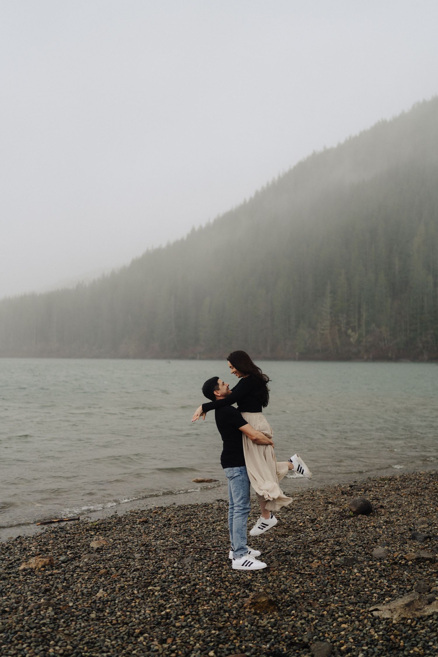 A romantic moment captured on a rocky beach with misty mountain backdrop.