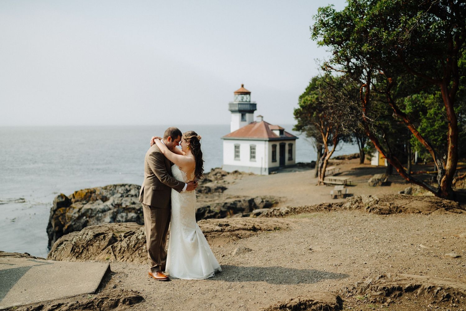 Romantic wedding photos captured near a white lighthouse on rugged coastal cliffs.