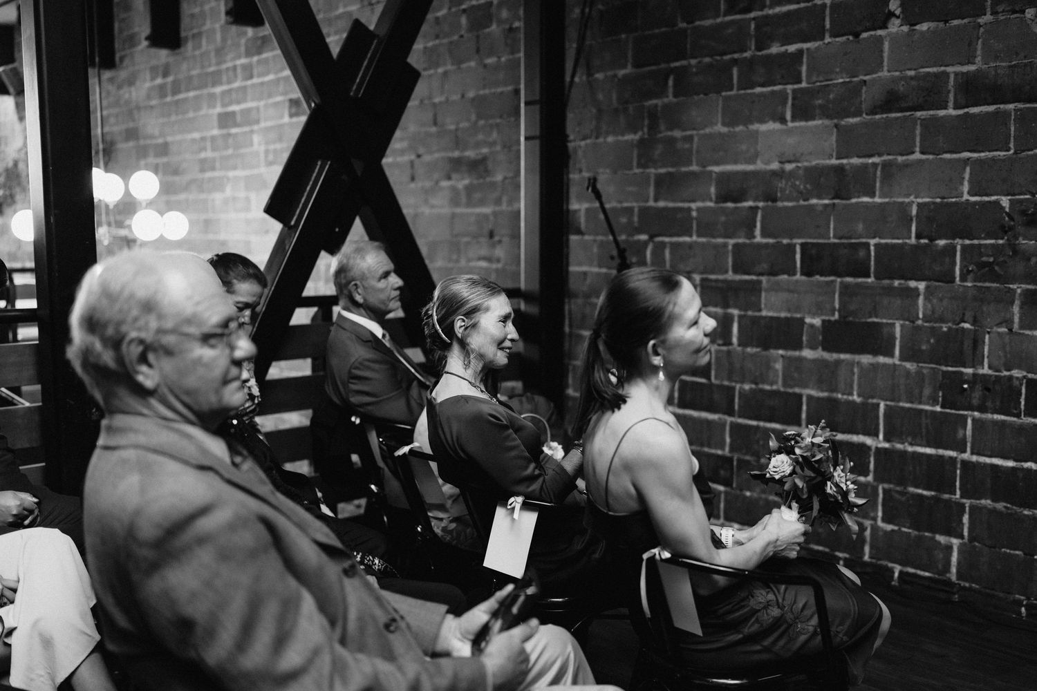 Wedding guests seated in rows watch the ceremony against an industrial brick backdrop.