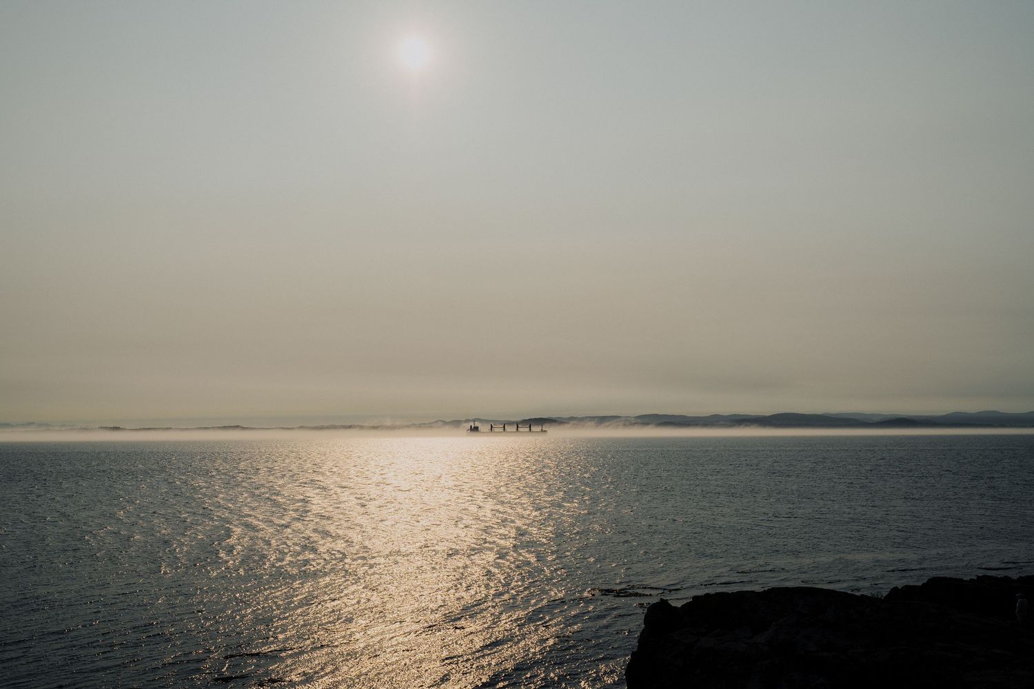 Serene sunset view over a calm ocean with misty horizon and glowing sun reflecting on the water.