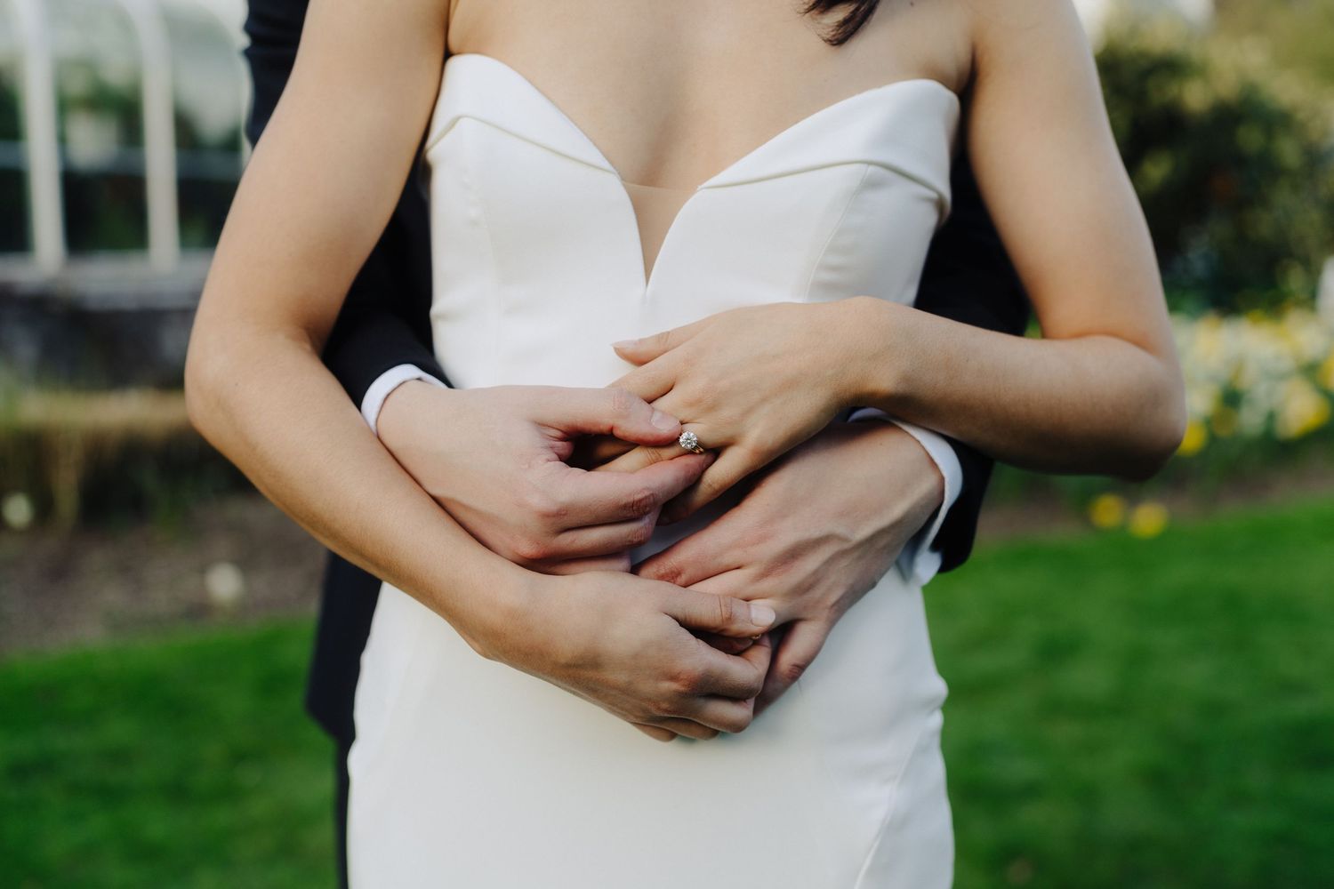 Close up shot of embracing hands around a white wedding dress waist.