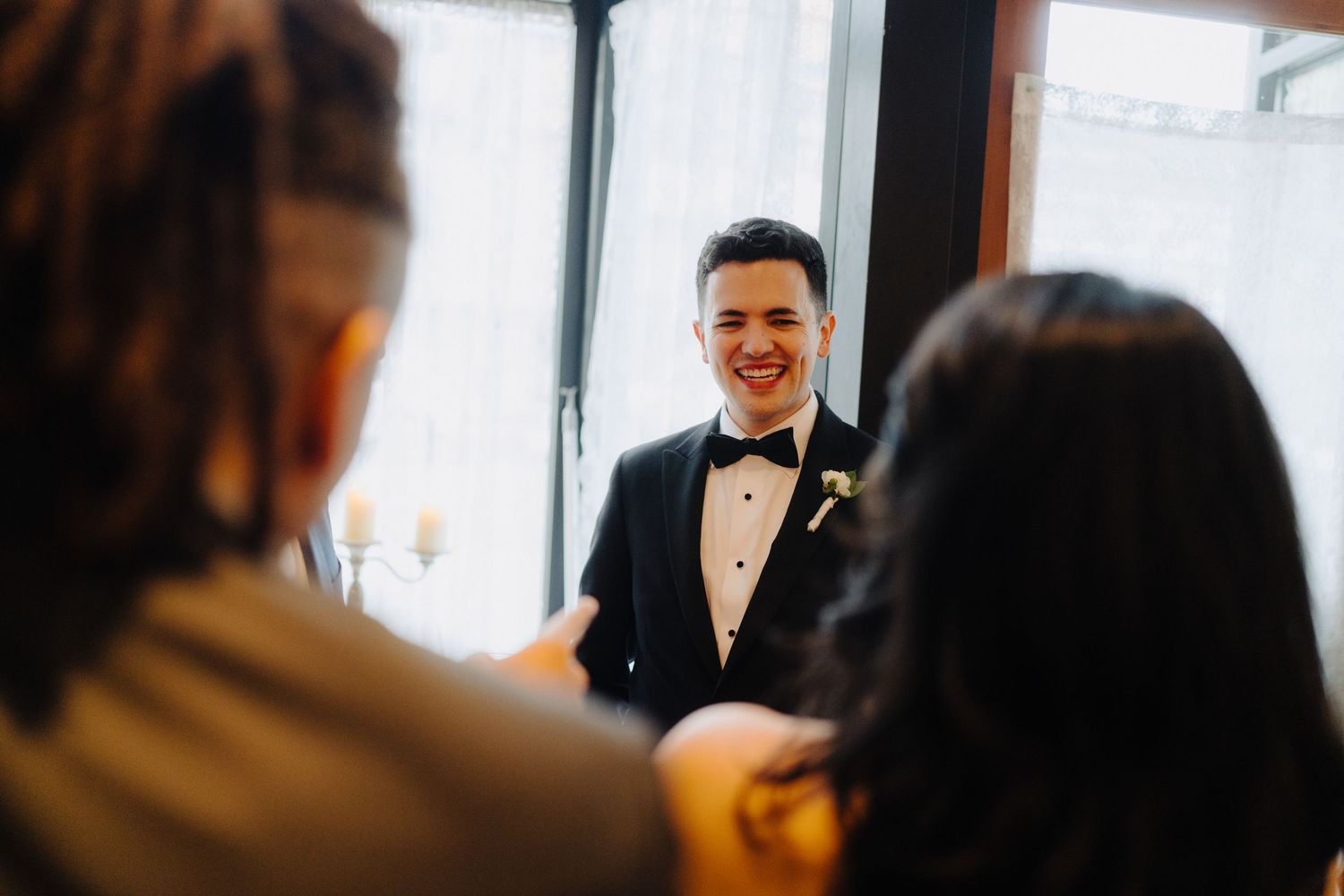 Happy groom in bow tie and tuxedo laughing during wedding celebration.