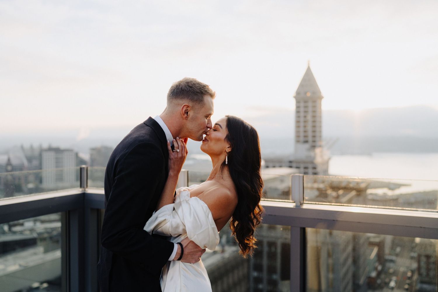 Romantic wedding couple sharing an intimate moment on a city rooftop terrace with iconic tower in background.