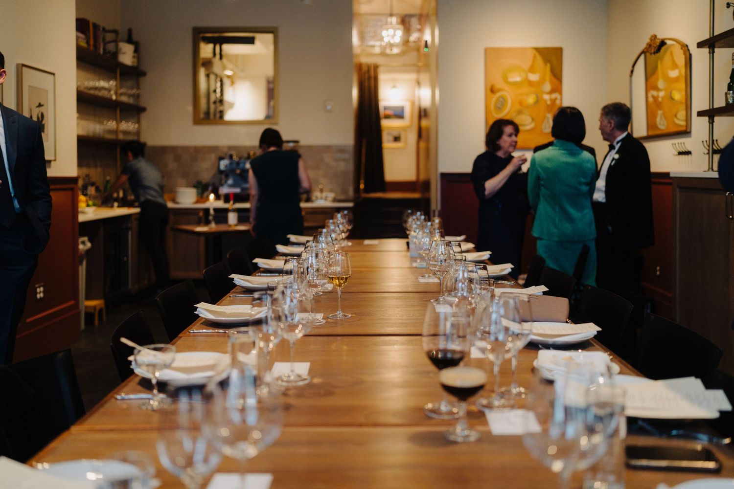 Long dining table set with wine glasses and white plates in an upscale restaurant interior.