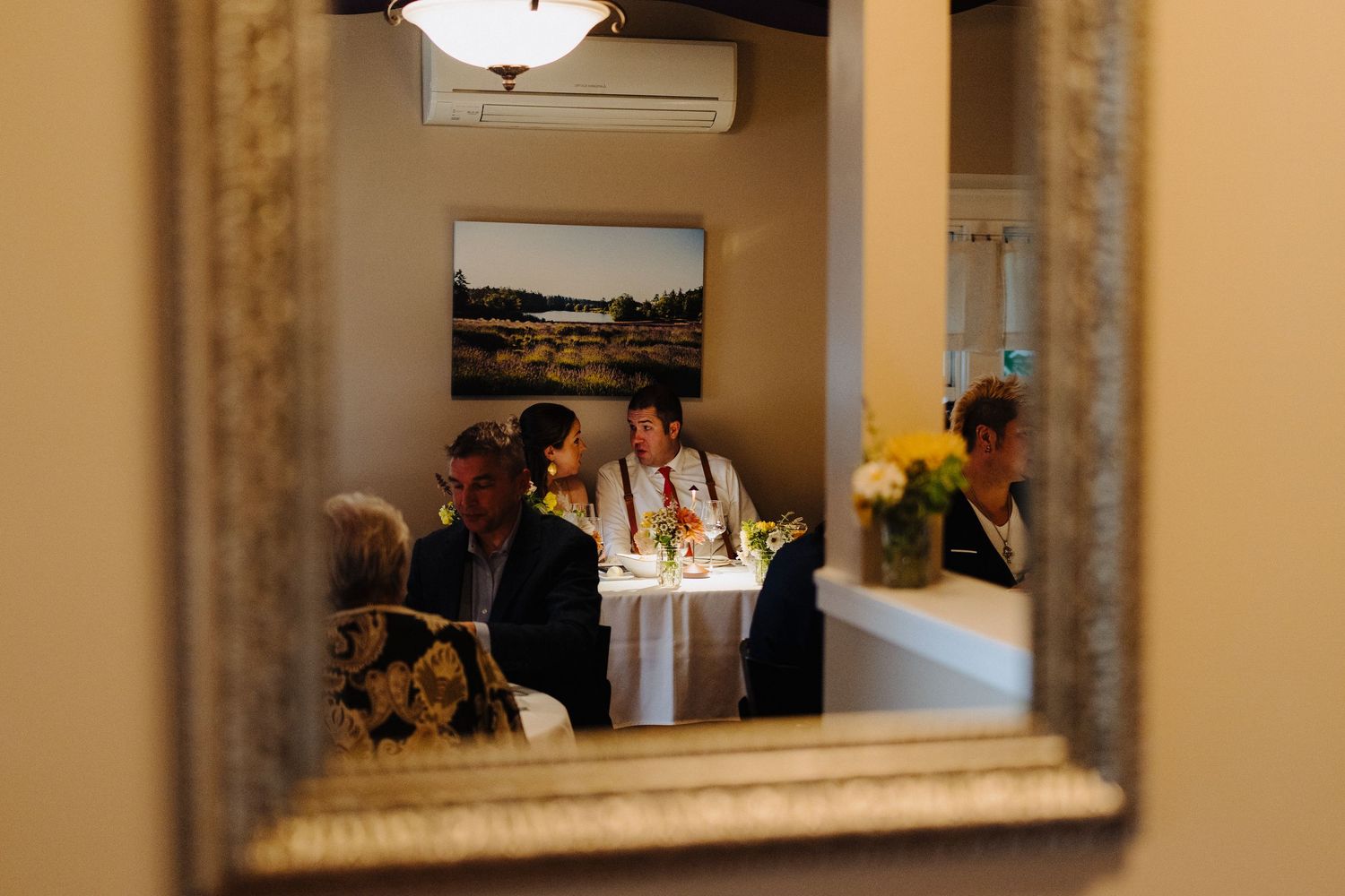 A reflection in an ornate mirror shows wedding guests dining at an elegant table.
