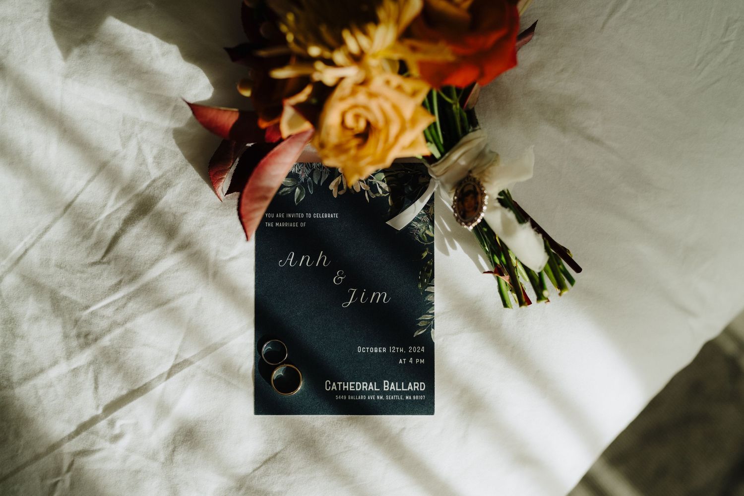 Wedding invitation and floral bouquet with orange and yellow roses on white fabric.