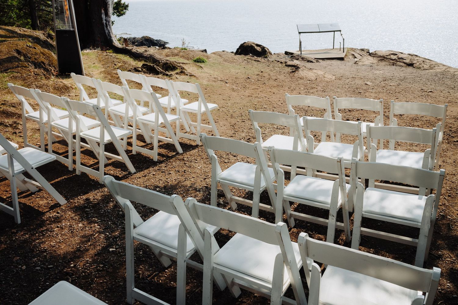 White wedding chairs arranged on a rocky hillside overlooking the ocean for an outdoor ceremony.
