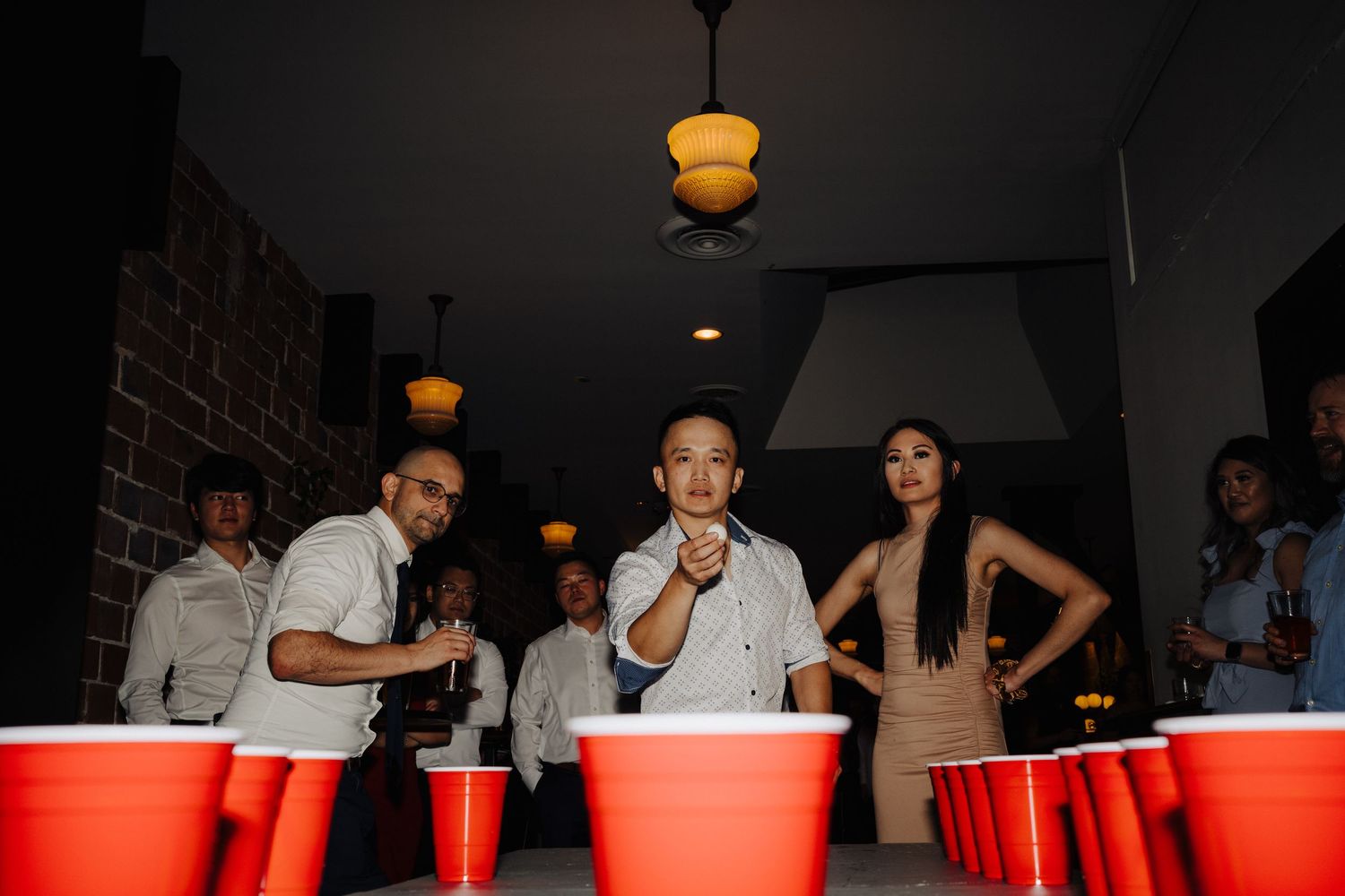 Party guests playing beer pong game with red cups at wedding reception.