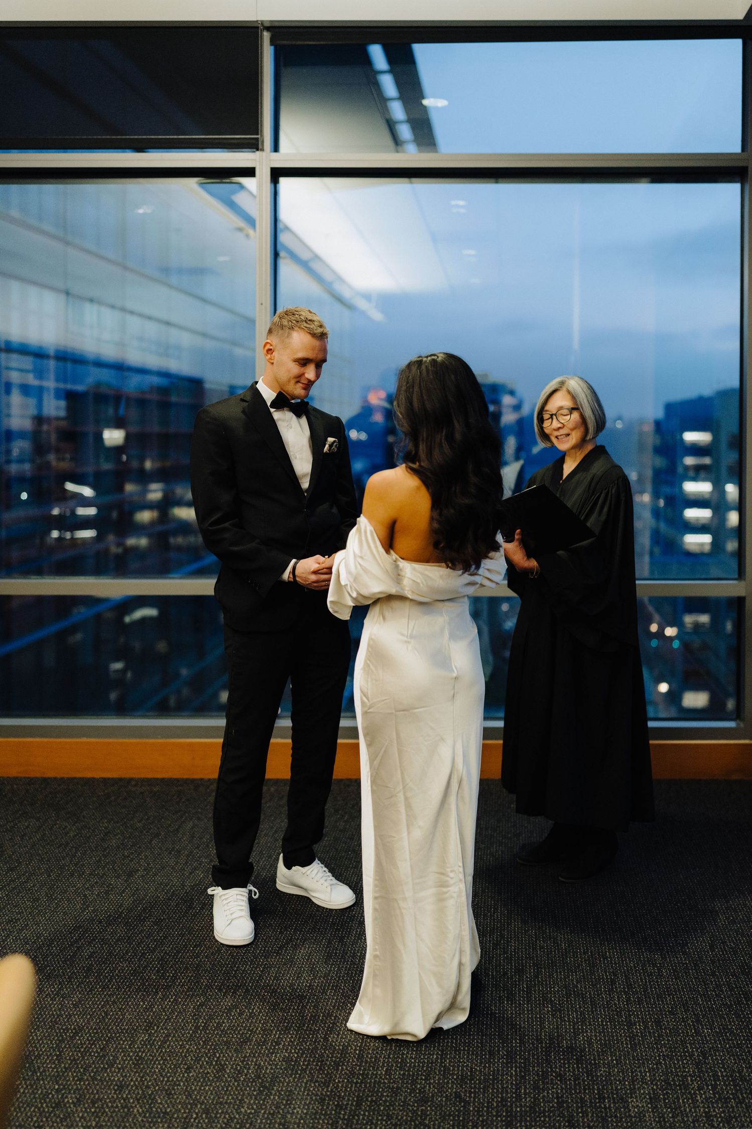 Small wedding ceremony taking place at sunset in front of city windows with mountain backdrop.
