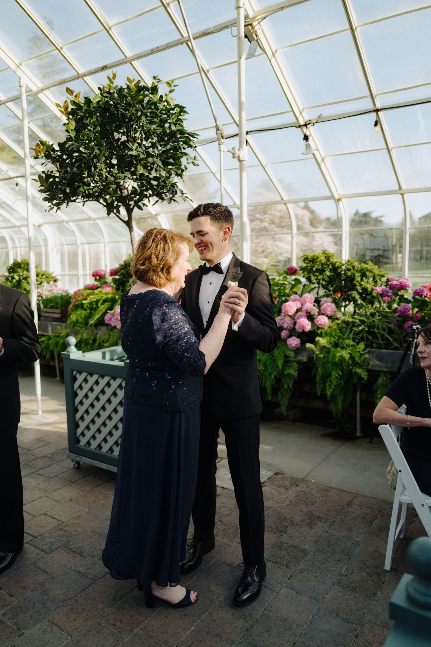 Sweet dance moment captured in a greenhouse wedding venue with pink flowers in the background.