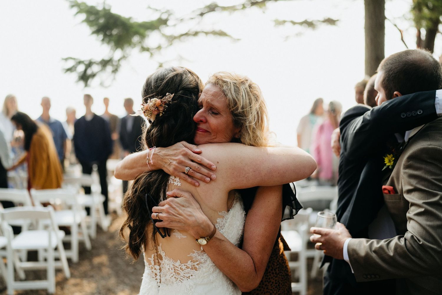Emotional embraces shared during an outdoor wedding ceremony with guests looking on.