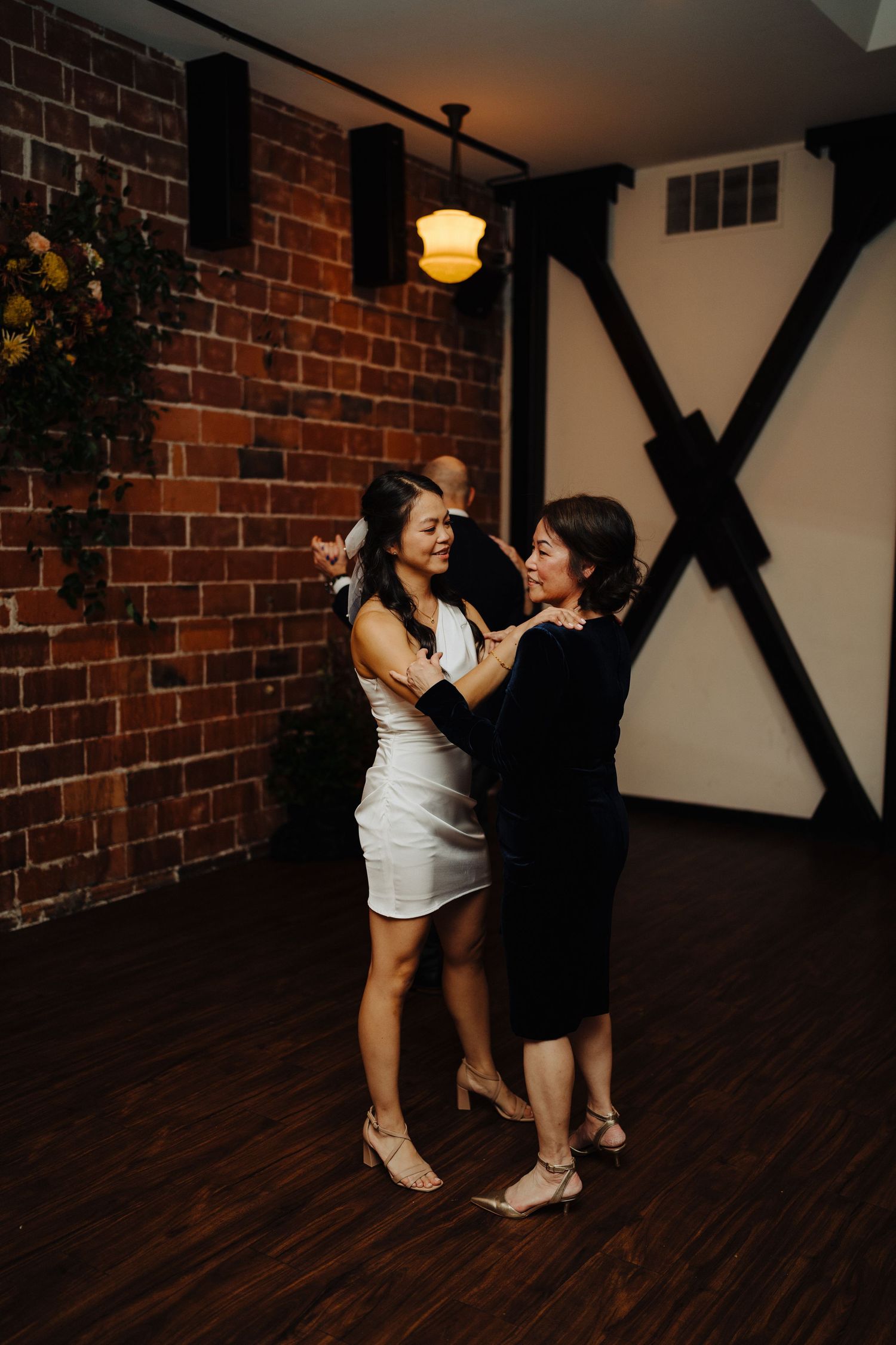 Two people share an intimate dance moment in a rustic venue with exposed brick walls.