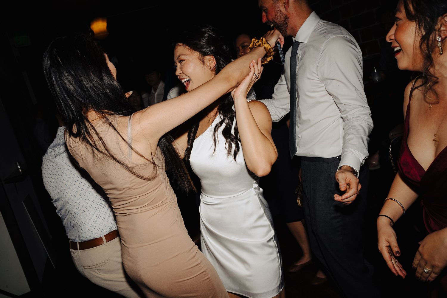 Wedding guests dancing and celebrating on a dimly lit dance floor.