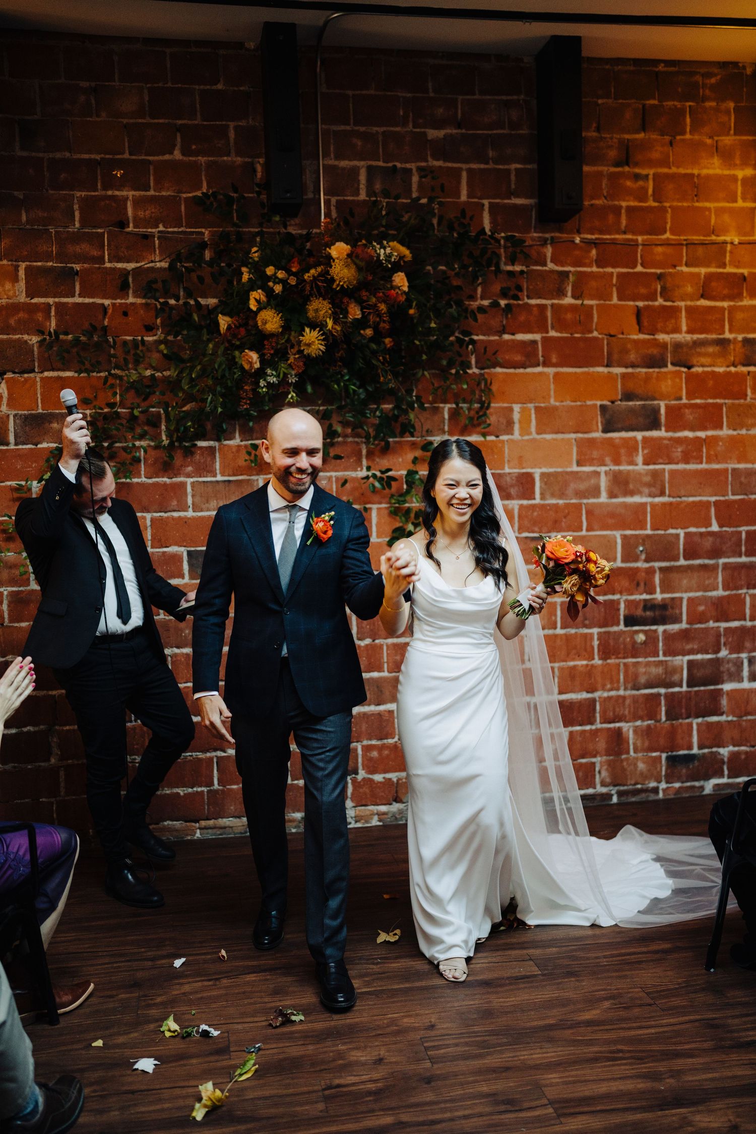 A joyful wedding celebration in a rustic brick-walled venue decorated with floral arrangements.