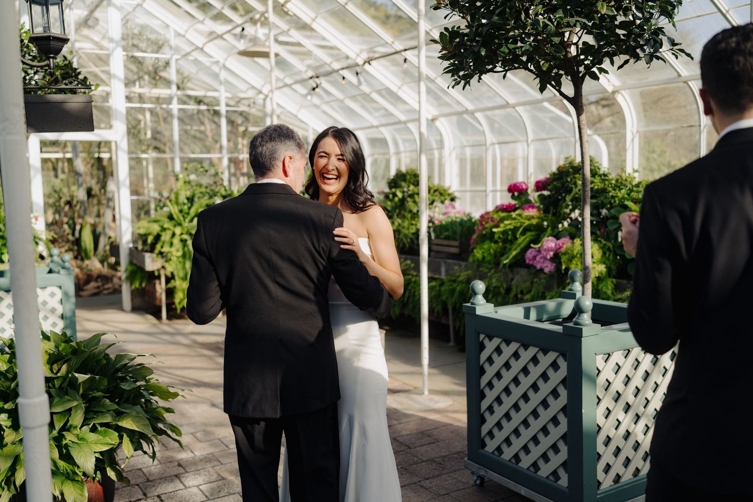 Newlyweds share an intimate moment in a sunlit greenhouse surrounded by lush greenery.