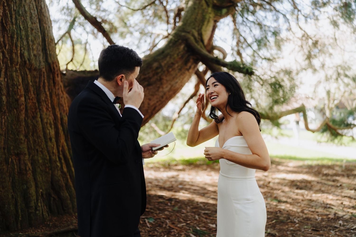 A couple shares an emotional first look moment under a majestic tree in a natural outdoor setting.