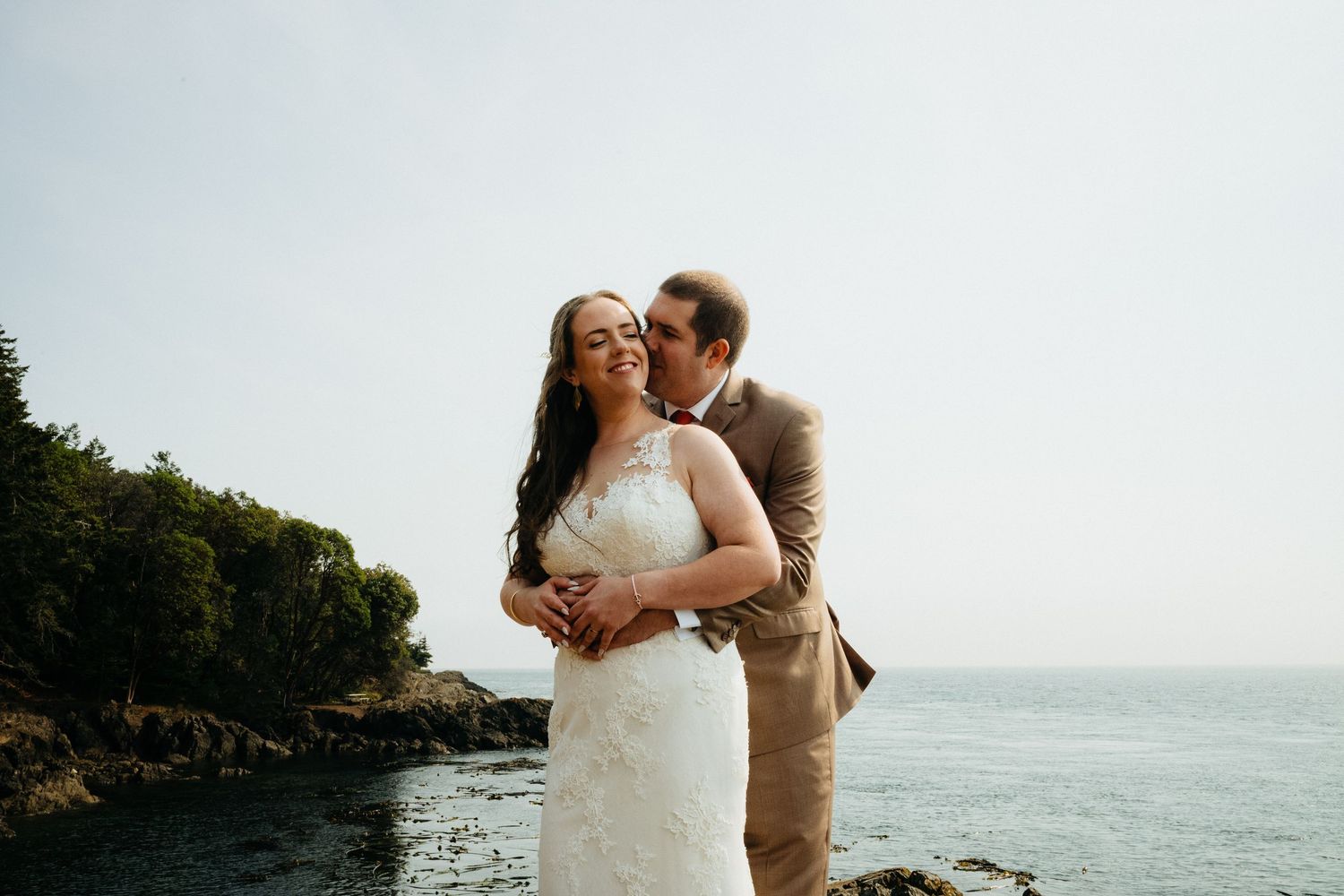 Couple sharing intimate moments against dramatic coastal backdrop with lighthouse.