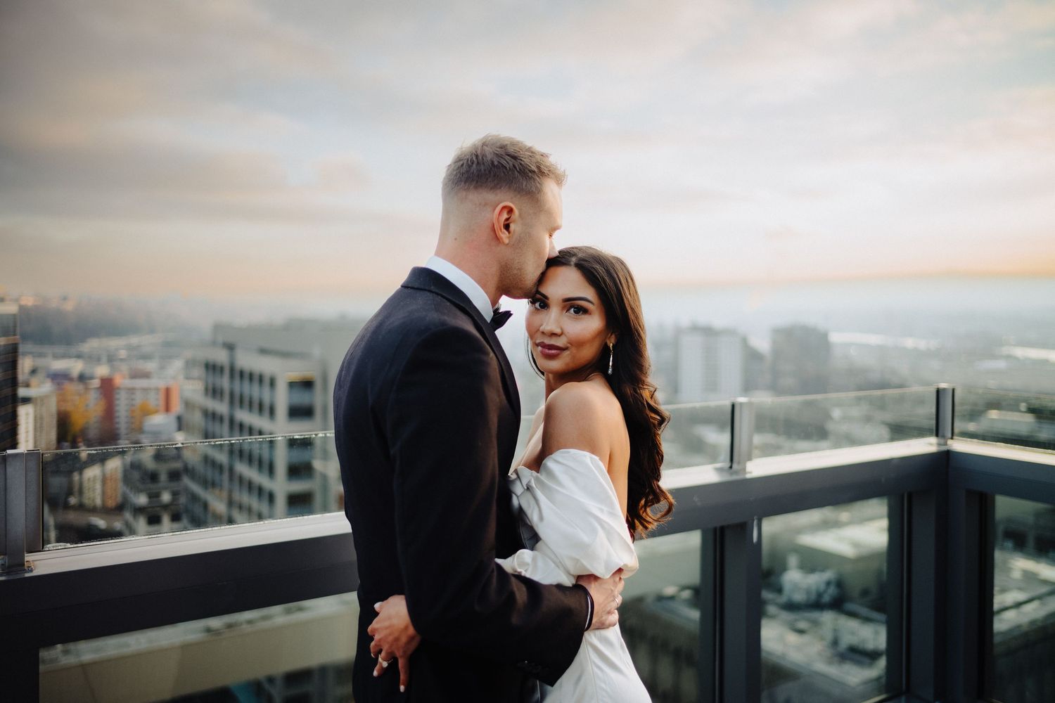 A couple shares a romantic moment on a rooftop terrace with urban skyline views.