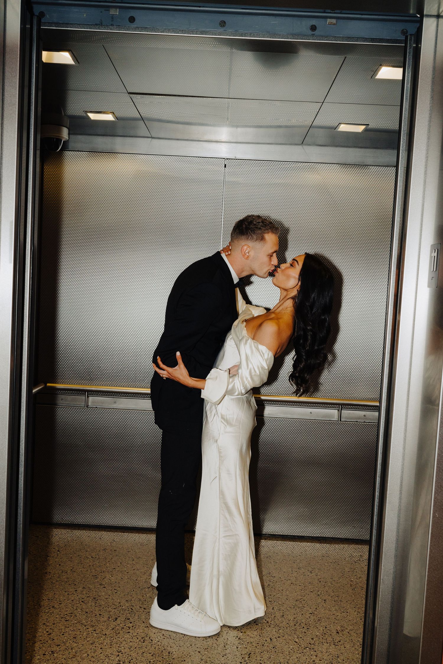 A couple sharing an intimate moment in an elevator while dressed in wedding attire.